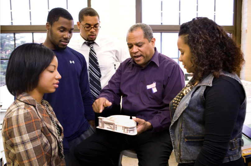 Robert Easter in a purple shirt holding an architectural model encircled by 4 students